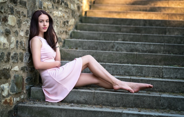Нежная девушка в розовом платье сидит на ступеньках 
