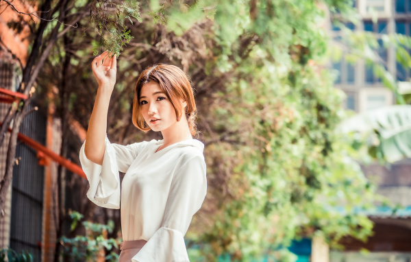 Молодая азиатка в белой блузке стоит у дерева 