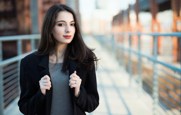 Молодая девушка в черном пальто стоит на мосту