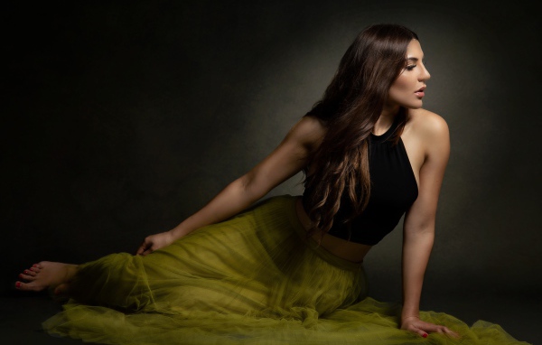 Молодая девушка в длинной юбке сидит на полу