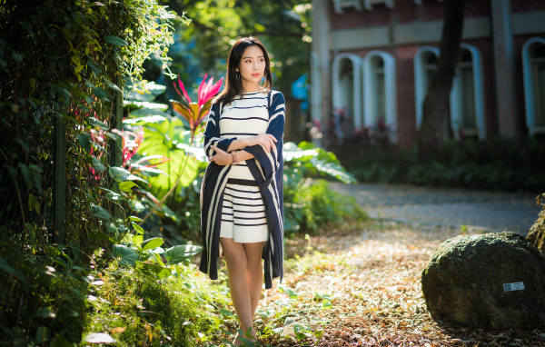 Девушка азиатка идет по улице у забора