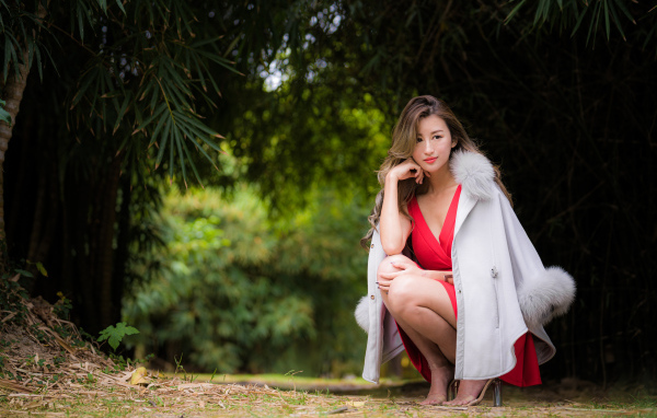 Азиатка в красном платье сидит в парке 