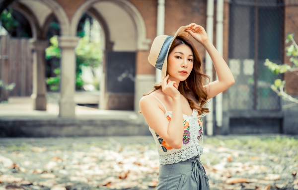 Красивая девушка азиатка в шляпе стоит в парке 