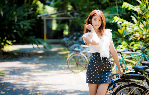 Красивая девушка азиатка в юбке в горох стоит у велосипеда 