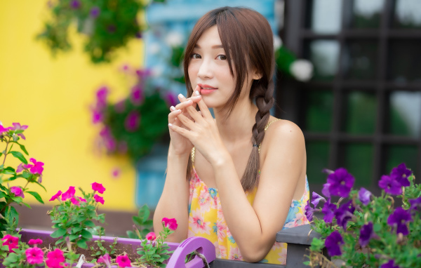 Красивая девушка Азиатка у цветов петунии