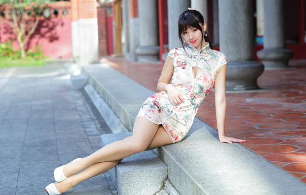 Красивая девушка азиатка в платье сидит на ступеньках