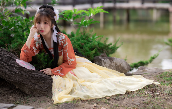 Красивая девушка азиатка сидит на земле у дерева 