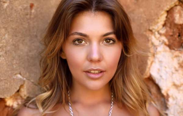 Красивая кареглазая девушка стоит у стены 