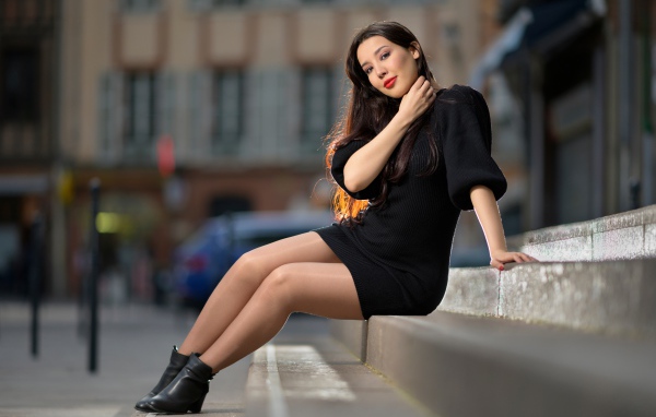 Красивая девушка в черном платье сидит на ступенях