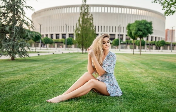 Красивая девушка в платье сидит на зеленом газоне 