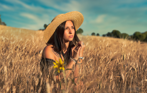 Красивая девушка в шляпе сидит на поле с пшеницей