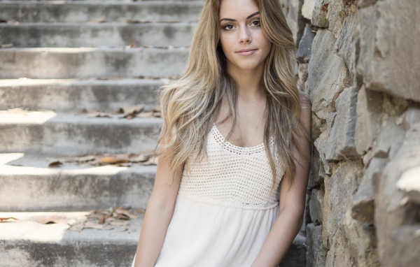 Красивая девушка в белом платье у каменной стены 