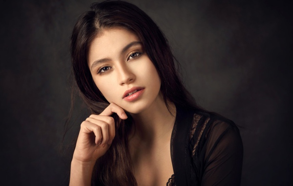 Красивая девушка в черном сидит на сером фоне