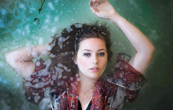 Красивая девушка лежит в одежде в воде 