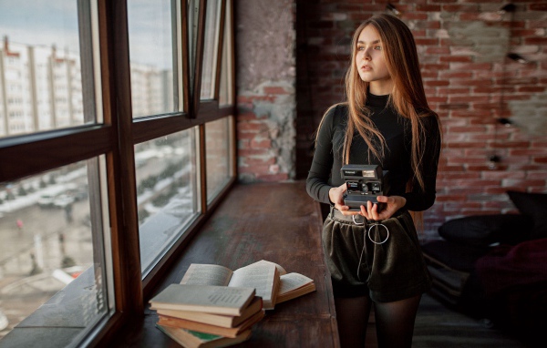 Красивая девушка с фотоаппаратом в руках у окна 