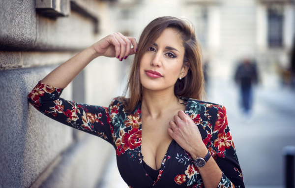 Красивая девушка с часами на руке стоит у стены