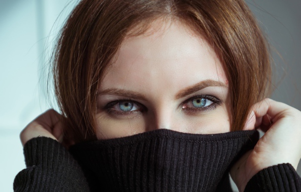 Красивая девушка с голубыми глазами закрыла лицо свитером 