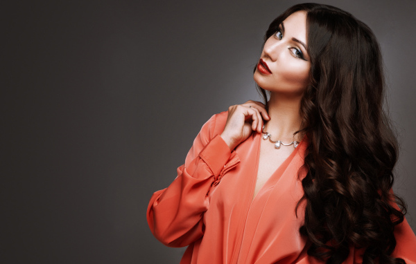 Красивая длинноволосая девушка в красной рубашке на сером фоне 