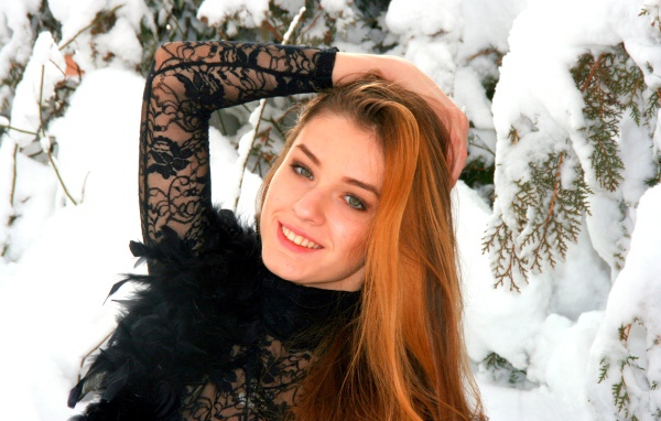 Красивая рыжеволосая девушка у заснеженной туи