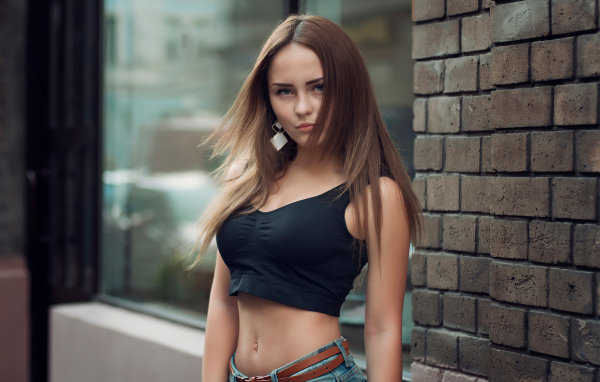 Красивая стройная девушка в черном топе стоит у стены