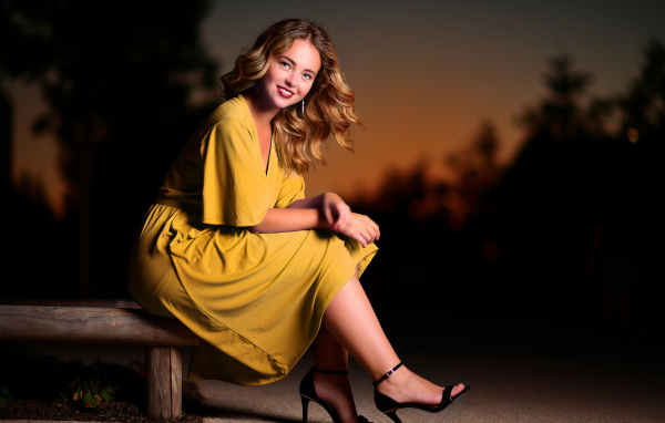 Красивая улыбающаяся девушка в желтом платье сидит на лавке 