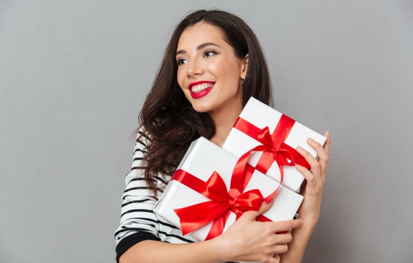 Красивая улыбающаяся девушка с подарками в руках на сером фоне 