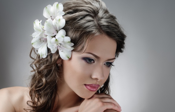 Красивая нежная девушка с белыми цветами в волосах на сером фоне
