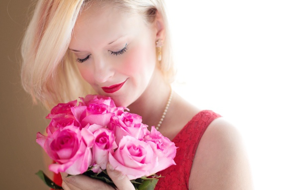 Блондинка с закрытыми глазами нюхает букет роз