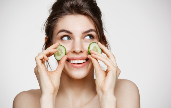 Голубоглазая девушка прикладывает огурцы к лицу 