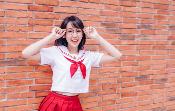 Яркая веселая азиатка в очках у кирпичной стены