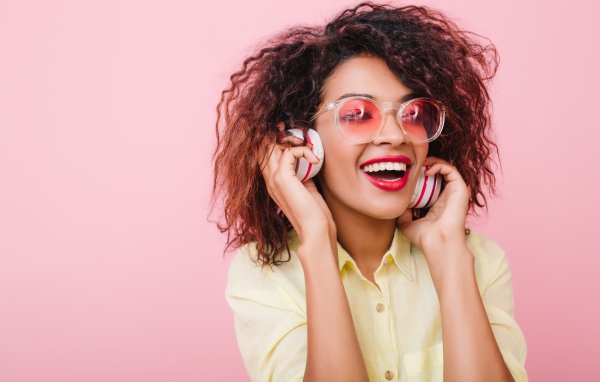 Яркая улыбающаяся девушка слушает музыку в наушниках 