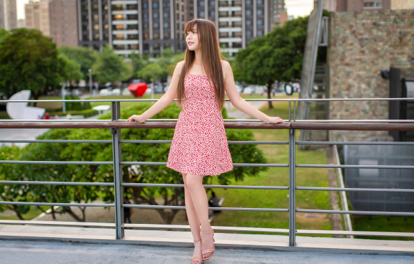 Милая девушка азиатка в платье стоит у перил 