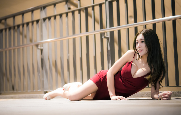 Милая девушка азиатка в красном платье лежит на земле