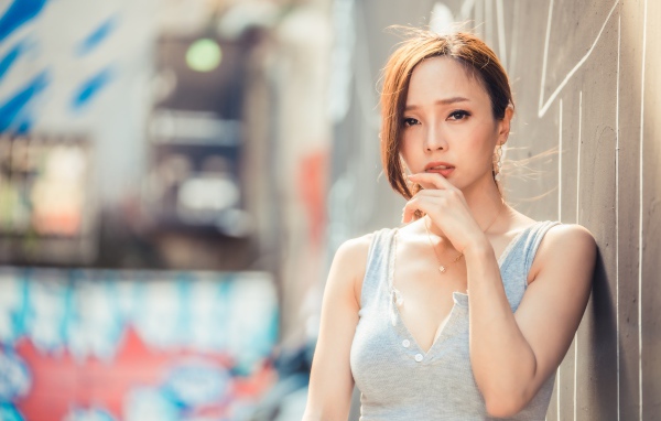 Милая девушка азиатка  с рукой у лица стоит у стены 