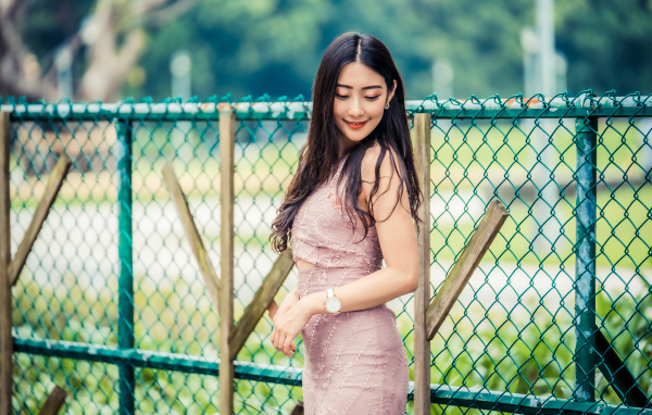 Милая азиатка в платье стоит под забором