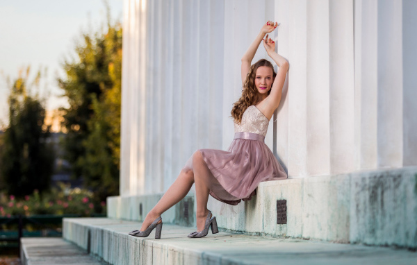 Милая девушка в юбке сидит на ступеньках у здания 