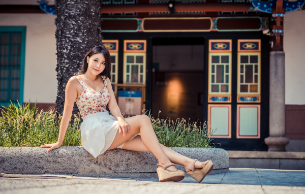 Милая улыбающаяся девушка сидит на бордюре