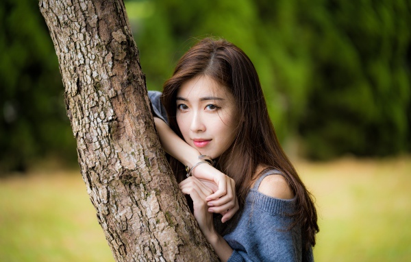 Мечтательная девушка азиатка стоит у дерева