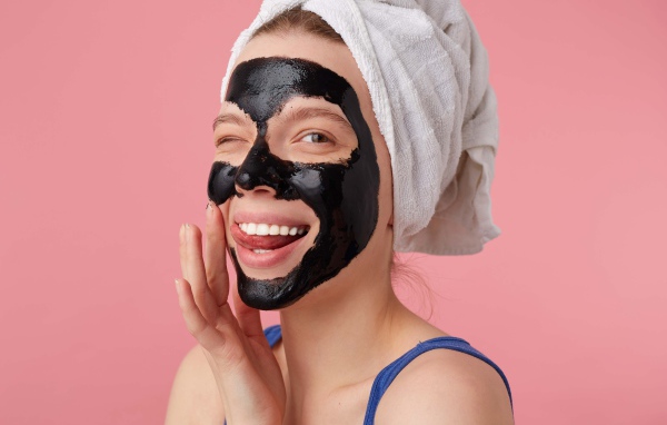 Смешная молодая девушка с черной косметической маской на лице 