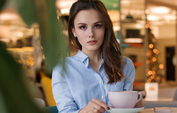 Girl in a blue shirt with a cup of coffee on a table in a cafe