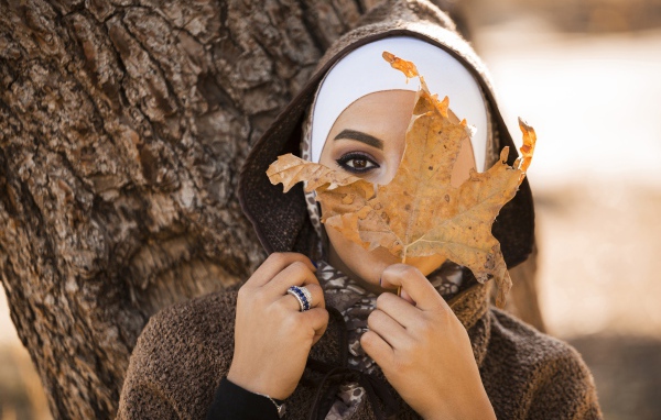 Девушка в пальто с закрывает лицо листом