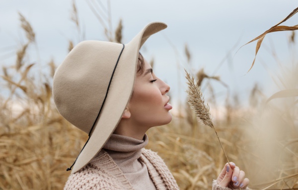 Девушка в шляпе с закрытыми глазами держит колосок 