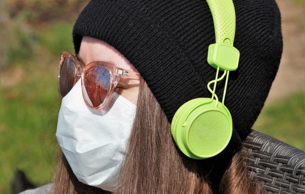 Девушка в медицинской маске на лице, в черной маске и наушниках