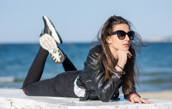 Девушка в черных очках и кожаной куртке на фоне моря
