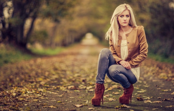 Девушка на высоких каблуках сидит на корточках в парке