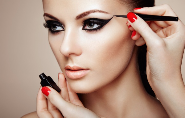 Девушке красят глаза черной подводкой 