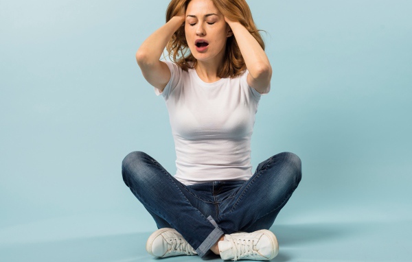 Девушка с руками в волосах сидит в джинсах на голубом фоне