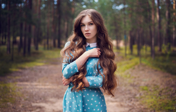 Длинноволосая девушка в голубом платье стоит в лесу