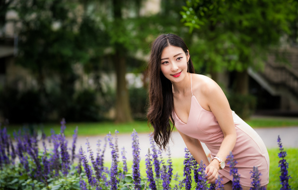 Милая девушка Азиатка в розовом платье у синих цветов