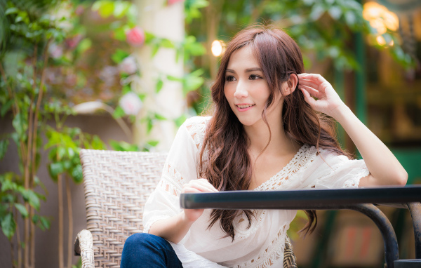 Улыбающаяся девушка азиатка сидит за столом в кафе